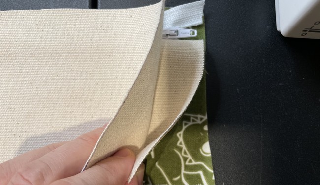 Bottom: lining piece right side up, zipper (with teeth facing up), top: outer fabric (right side down). The other panels that you sewed in step 4 will be tucked in between these layers